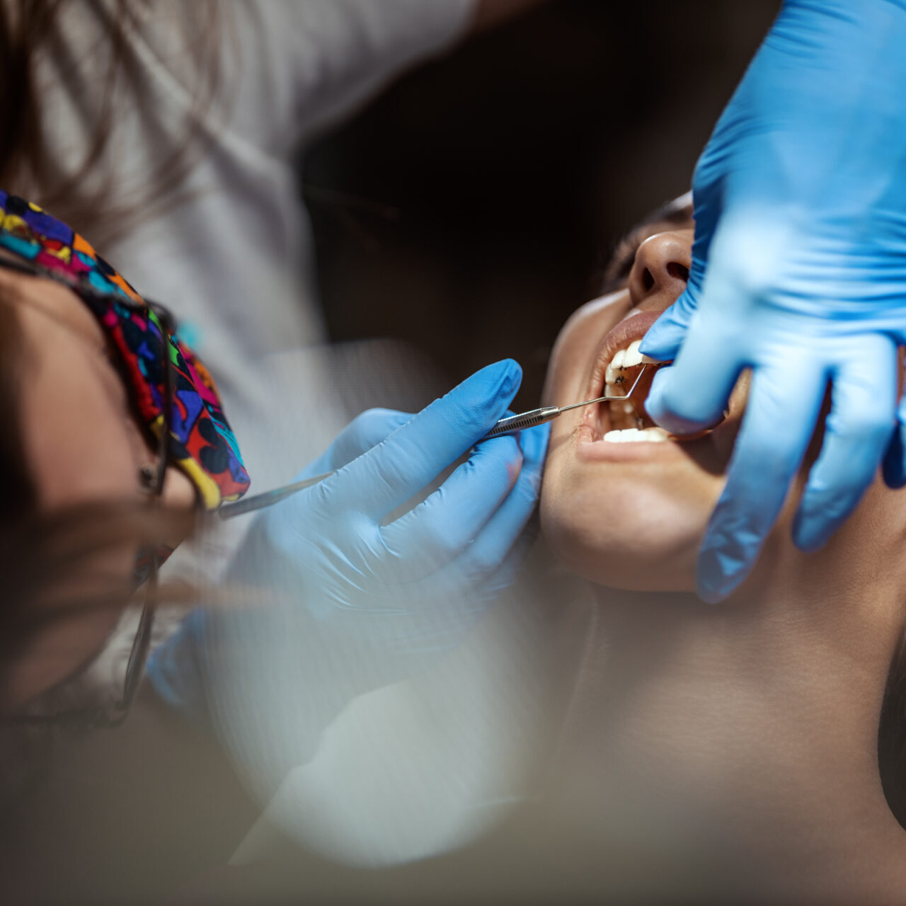 The beautiful young woman is at the dentist. She sits in the dentist's chair and the dentist sets braces on her teeth putting aesthetic self-aligning lingual locks.